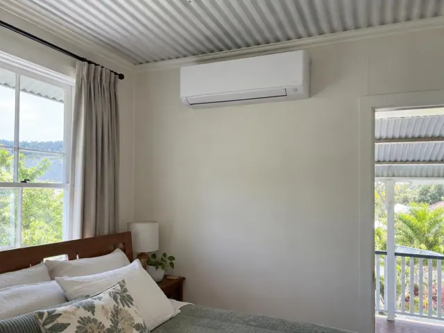 Split system indoor unit mounted high on a bedroom wall with curtains and a window in Mudgeeraba